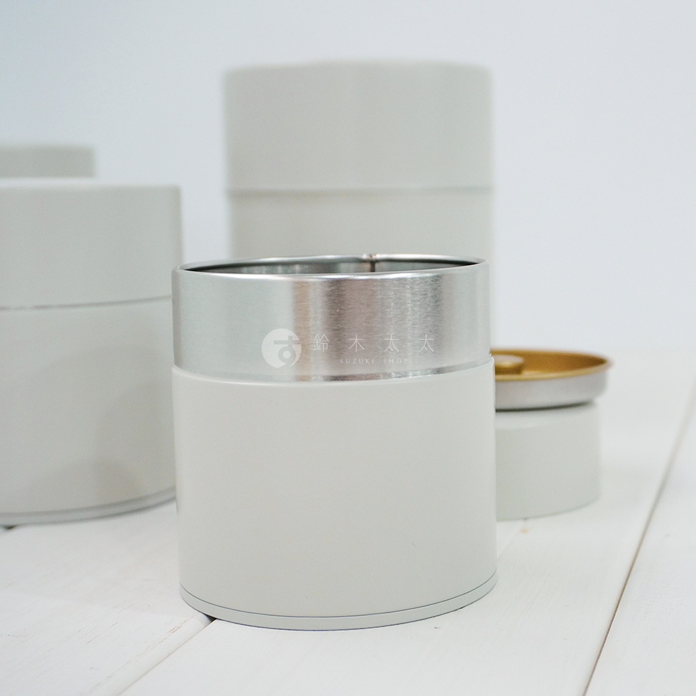簡約風格的錫製茶葉罐，罐身為淺灰色，頂部飾有銀色金屬環，環上印有「鈴木太太 SUZUKI SHOP」的品牌標誌。