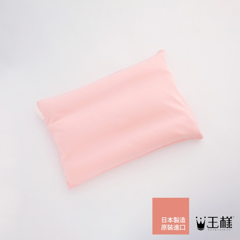 淡粉色枕頭，材質柔軟，表面平整，帶有細微的紋理，角落處有黃色小標籤，右下角有品牌標誌和日文說明。