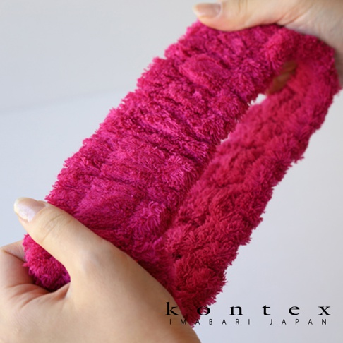 一條桃紅色毛巾材質的髮帶，質地柔軟蓬鬆，由雙手撐開展示。