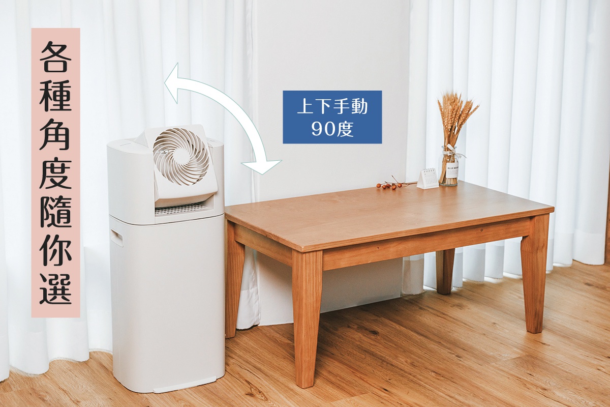 白色直立式循環除濕機，上方有可上下手動90度調節的風扇，擺放在木質地板上，旁邊有一張淺色木桌，桌上放有裝飾品。