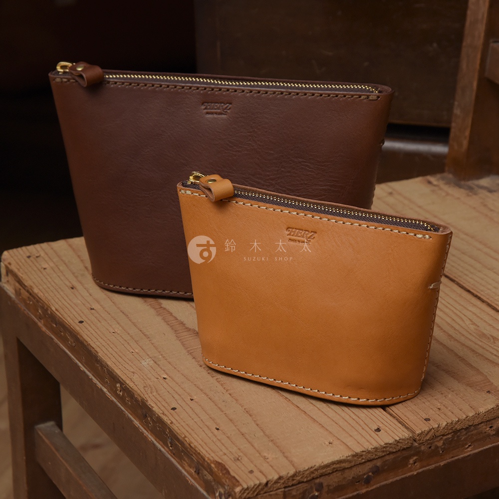 兩個皮革三角收納包，一個為深棕色，另一個為淺棕色，皆配有金色拉鍊和縫線。