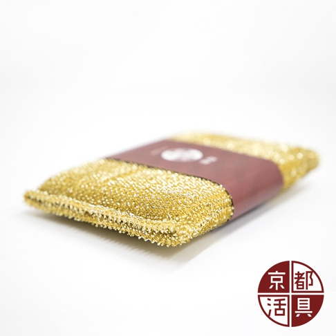 金黃色不沾鍋專用菜瓜布，表面為細密網狀材質，中間以深紅色紙質包裝帶束起，包裝帶上有白色標誌。