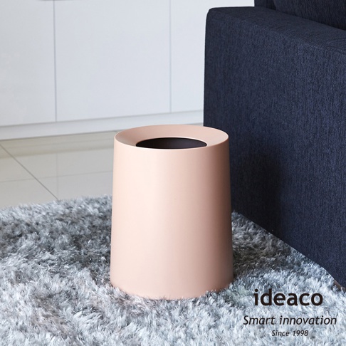 粉色圓形家用垃圾桶，容量11.4公升，採用光滑的塑膠材質，桶身呈錐形，開口朝上，放置於灰色長毛地毯上，背景為深藍色沙發和白色廚櫃。