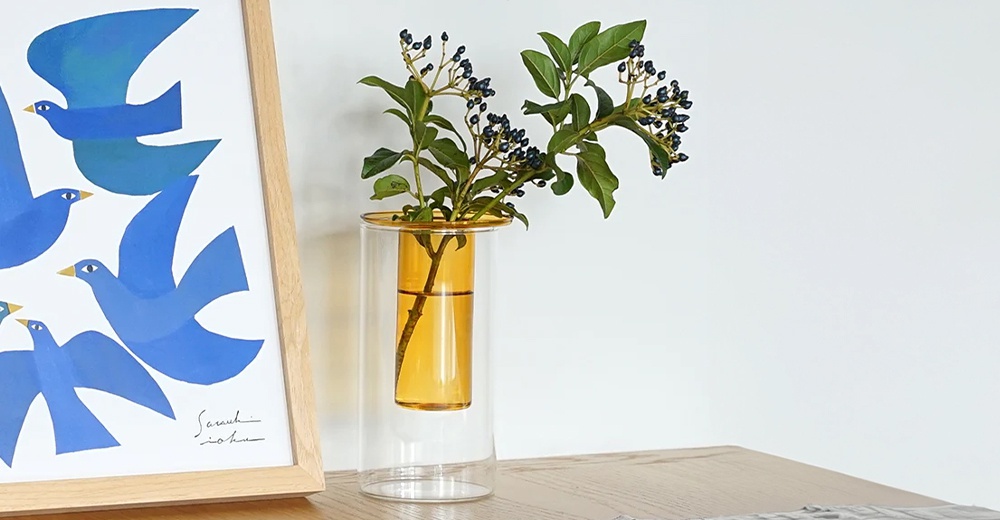 AXCIS PINO 雙層可拆玻璃花瓶高款，搭配藍色飛鳥圖畫與綠葉裝飾，擺放在木桌上