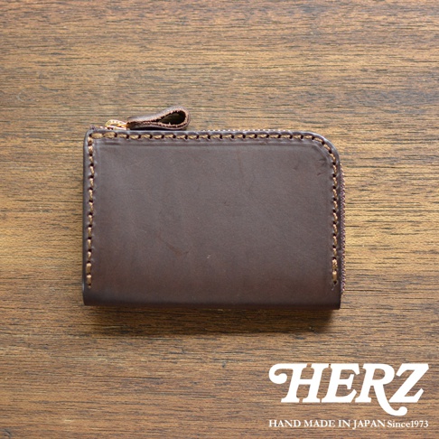 深棕色皮革製的短夾，配有金色拉鍊和同色皮革拉環，邊緣以咖啡色縫線裝飾，整體放在木紋桌面。