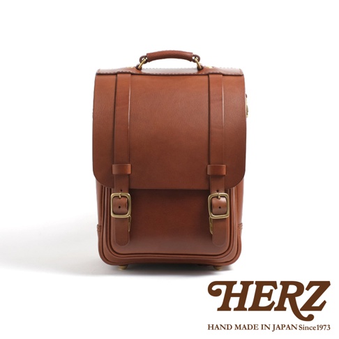 職人手作皮革小學生書包，經典棕色，採用高品質皮革製作，正面有兩條皮帶和兩組銅質扣環，設計簡潔大方。