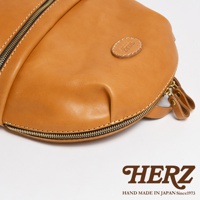 職人手作皮革圓角後背包，採用鞣製皮革材質，呈現溫潤的焦糖棕色。大開口設計，附有雙拉鍊頭，細緻車縫線與圓形皮革標誌，展現精緻工藝。