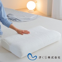 白色人體工學枕，表面有蜂巢狀紋理，枕套材質為透氣織物，一隻手輕柔地放在枕頭上，背景是臥室環境，有檯燈和床鋪。