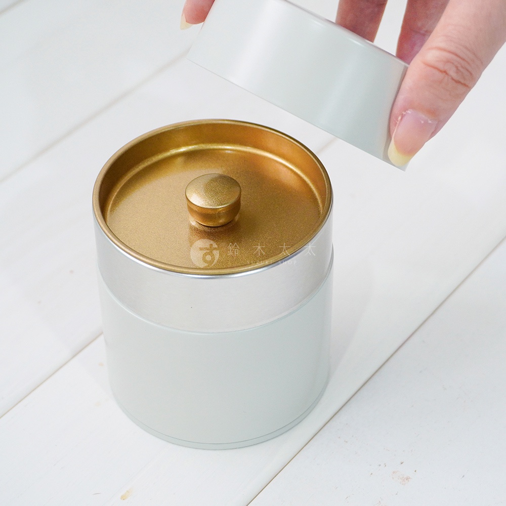 簡約錫製茶葉罐，罐身為淺灰色，帶有金色圓形提鈕的金色內蓋。