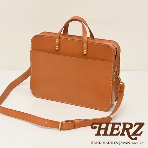 職人手作皮革兩用商務公事包，採用鞣製皮革製成，呈現溫潤的焦糖棕色。包款設計簡潔，正面設有大型插袋，頂部有提把，並配備可拆卸的肩背帶，適合商務使用。