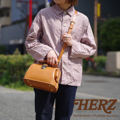 職人手作皮革方型迷你醫生包，採用光滑棕色皮革製作，配有銀色金屬鎖扣和可調節肩帶。包身底部有四個金屬釘腳。