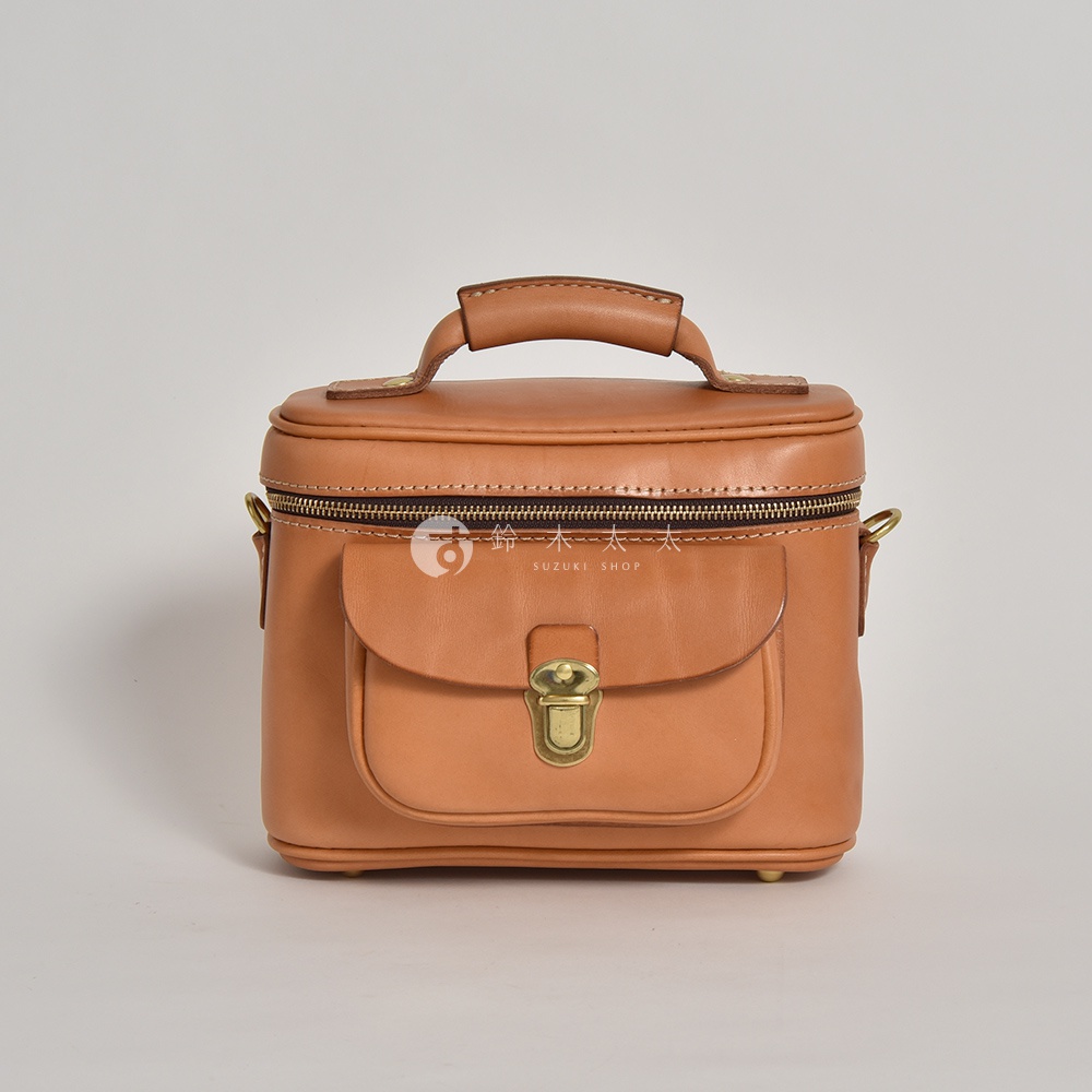 棕色皮革手提相機包，設有頂部提把、拉鍊開合、前方翻蓋口袋及金屬鎖扣。