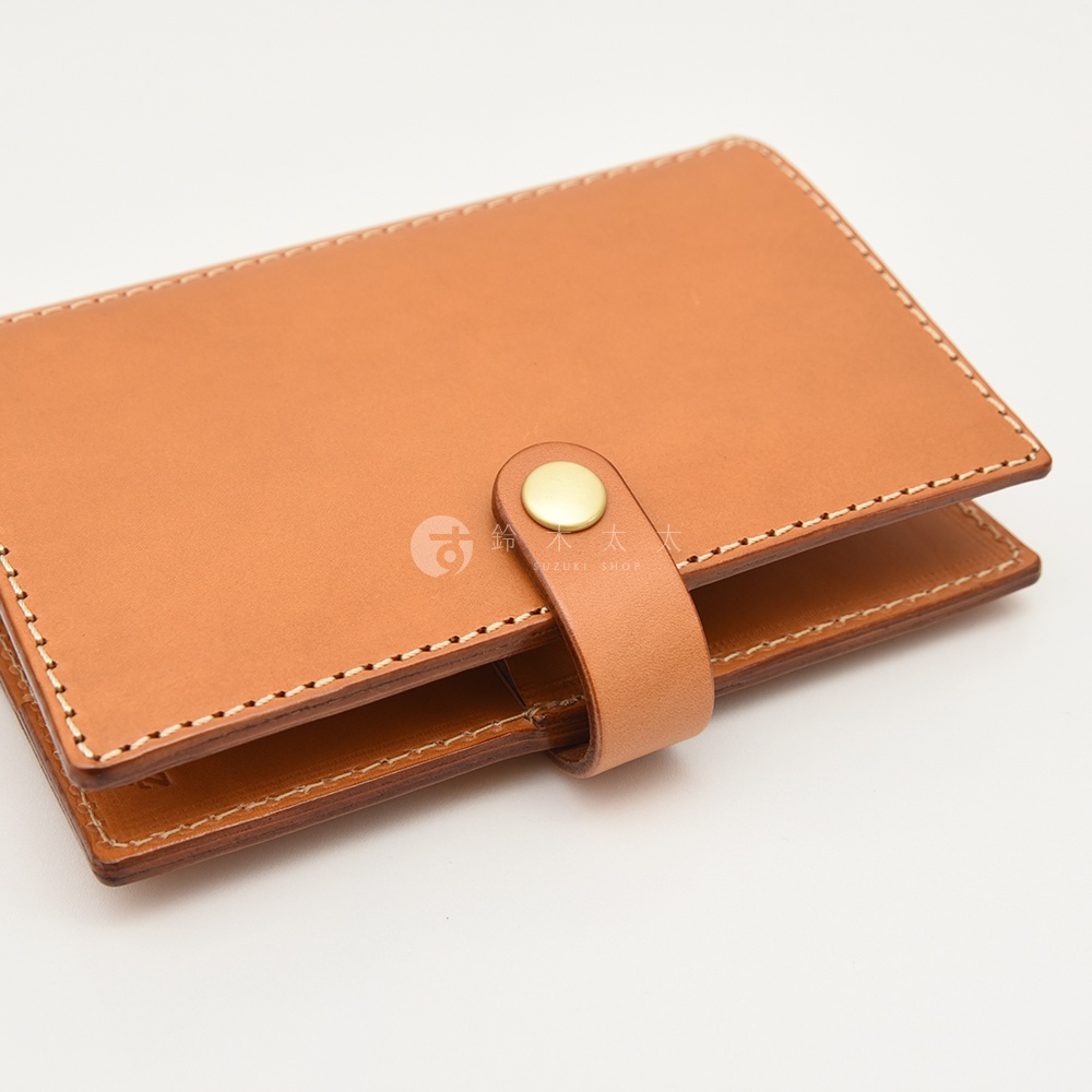 淺棕色皮革手帳/記事本書套，以白色縫線手工車縫，書套上有一個金屬按扣，用於固定書套。