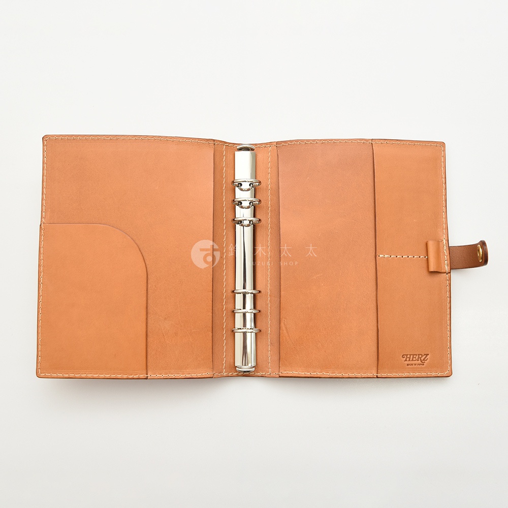 職人手作皮革A5手帳，淺棕色，打開狀態，內有兩個筆插、兩個卡槽、一個文件夾，以及銀色六孔活頁夾，右側有皮質束帶。