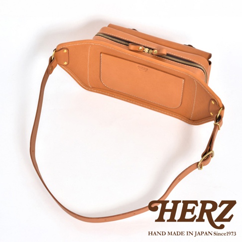 職人手作皮革騎士隨身斜背包，淺棕色皮革，有拉鍊開合、前置平口袋及可調整長度的斜背帶。