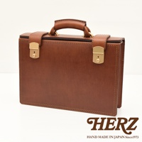 職人手作皮革機師箱，採用棕色皮革製成，配有金色鎖扣和提把，箱體線條簡潔，縫線清晰。