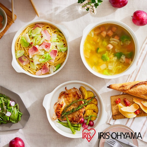 白色陶瓷不沾平底鍋盛裝義大利麵、湯品、烤雞與配菜，旁邊擺放麵包與水果，整體呈現豐盛的餐點畫面。