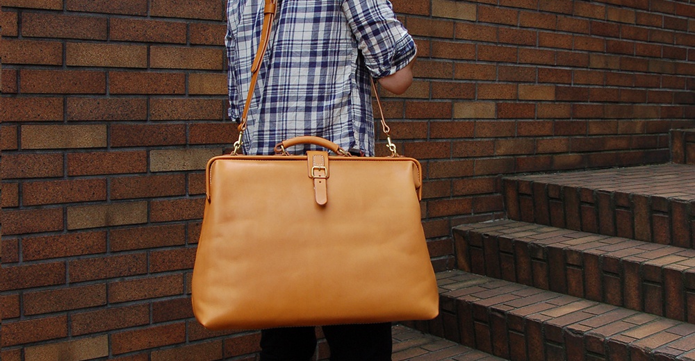 職人手作皮革軟式杜勒斯包，淺棕色，附有可調節肩帶和頂部提把，以金色金屬扣環固定。