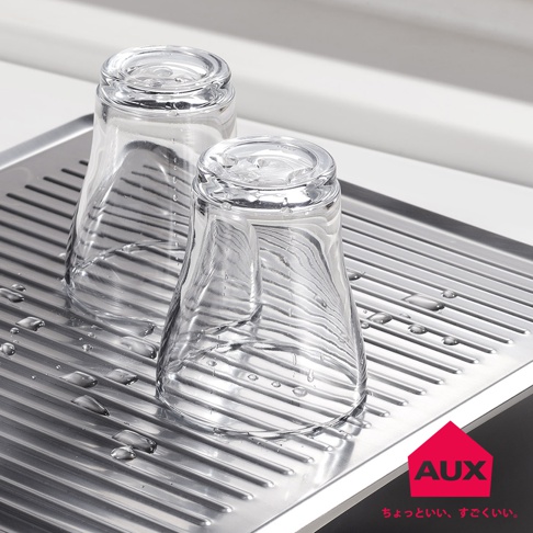 不鏽鋼瀝水盤上放置兩只透明玻璃杯，瀝水盤有條狀紋路，盤面上散落著水滴。