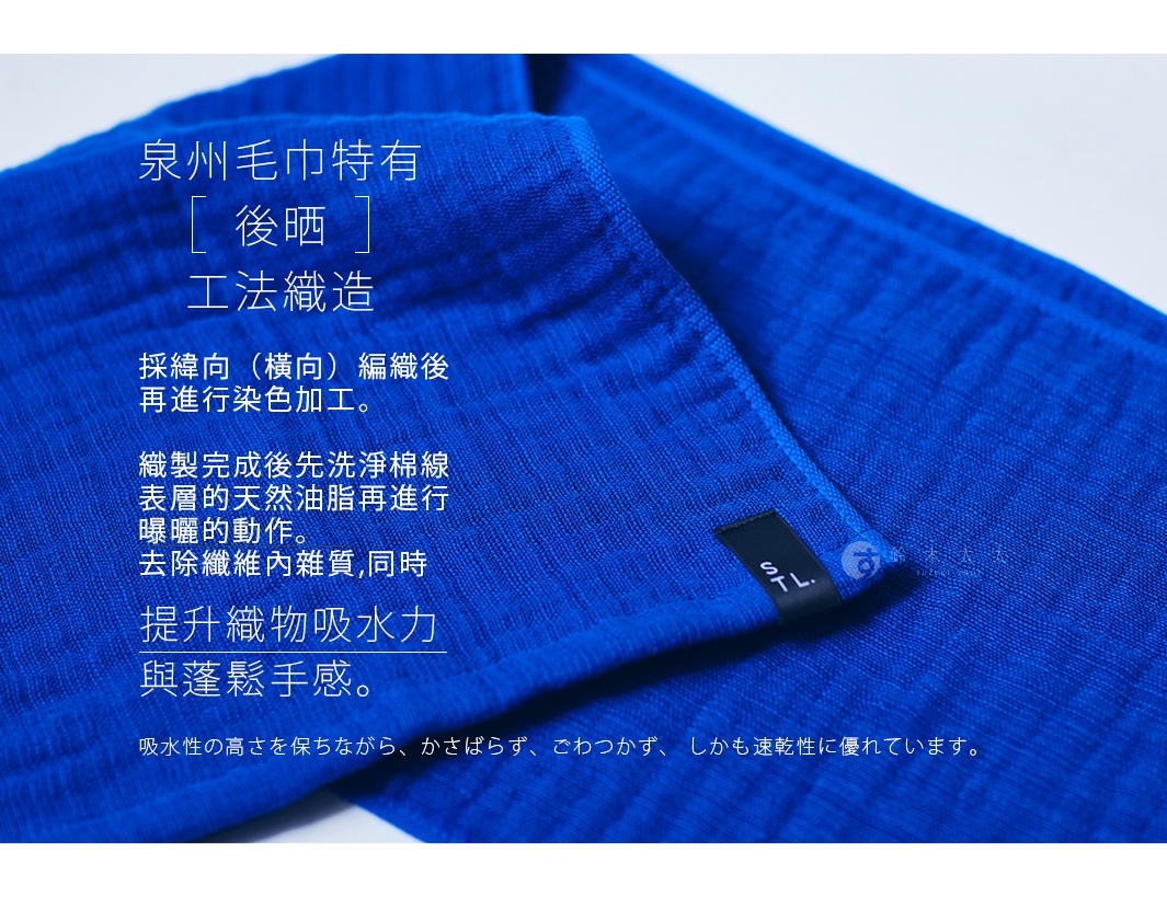 一塊鮮豔的藍色隨身暖毯，材質為2.5層紗，質地柔軟，表面可見細緻的織紋。暖毯一角縫有一個黑色標籤，上面印有「S TL.」字樣。