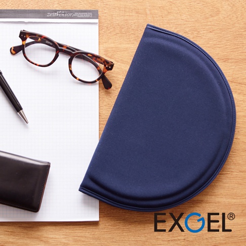 深藍色半圓形MINI PUNI Plus坐墊，布面材質，邊緣有縫線，置於木紋桌面，旁邊有筆記本、眼鏡及筆。