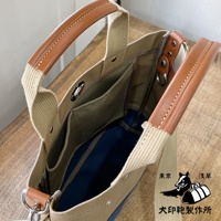 米色純棉帆布托特包，搭配棕色皮革提把及肩帶，內部有多個隔層，可見藍色內襯。