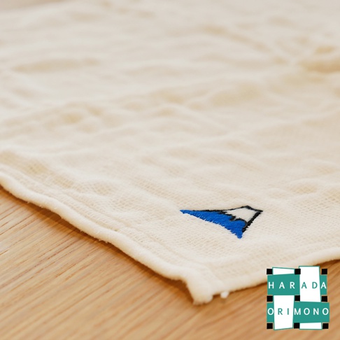 米白色八重紗精繡萬用吸水擦拭巾，織紋清晰，左下方繡有藍白相間的富士山圖案，質感柔軟，適合日常使用。
