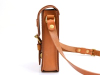 棕色皮革製成的經典皮扣單肩包，一側特寫，展示其材質、縫線、金屬扣環和可調節肩帶。