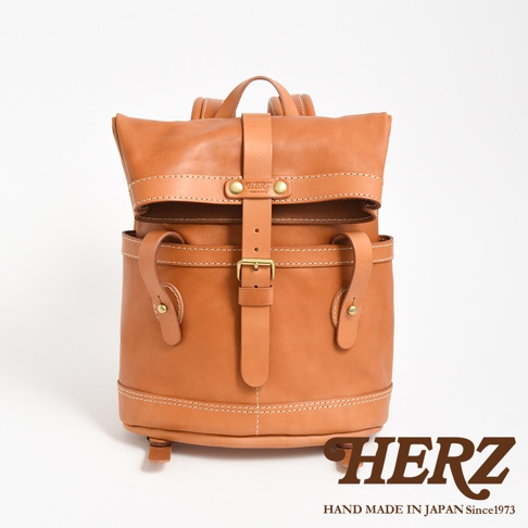 棕色皮革雙口袋折蓋後背包，設有皮帶和金屬扣環。