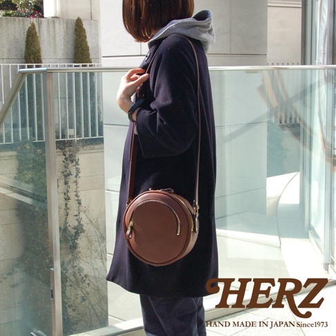 職人手作皮革小圓包，圓形包身，咖啡色皮革材質，配有金色拉鍊和金屬扣環，可肩背。