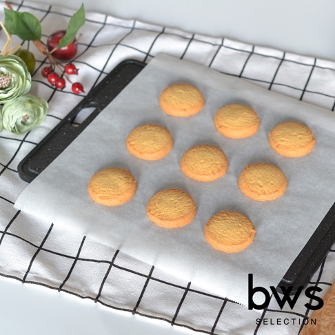 黑色食物快速冷卻盤上鋪著烘焙紙，擺放著九塊金黃色圓形餅乾，旁邊有綠色裝飾和紅色漿果。