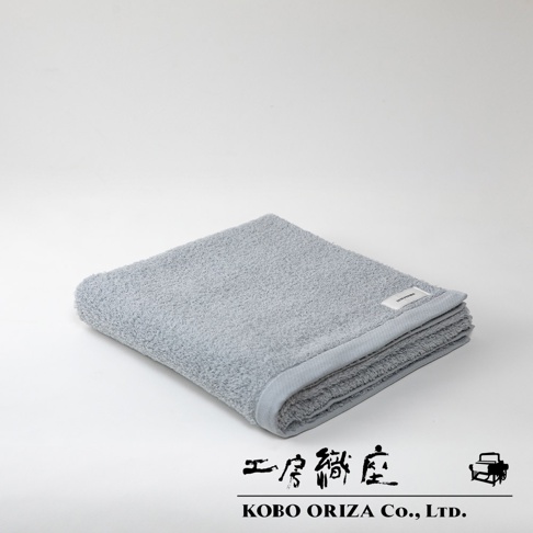 一條淺灰色、觸感柔軟的超細纖維浴巾，整齊對折，帶有品牌標籤。