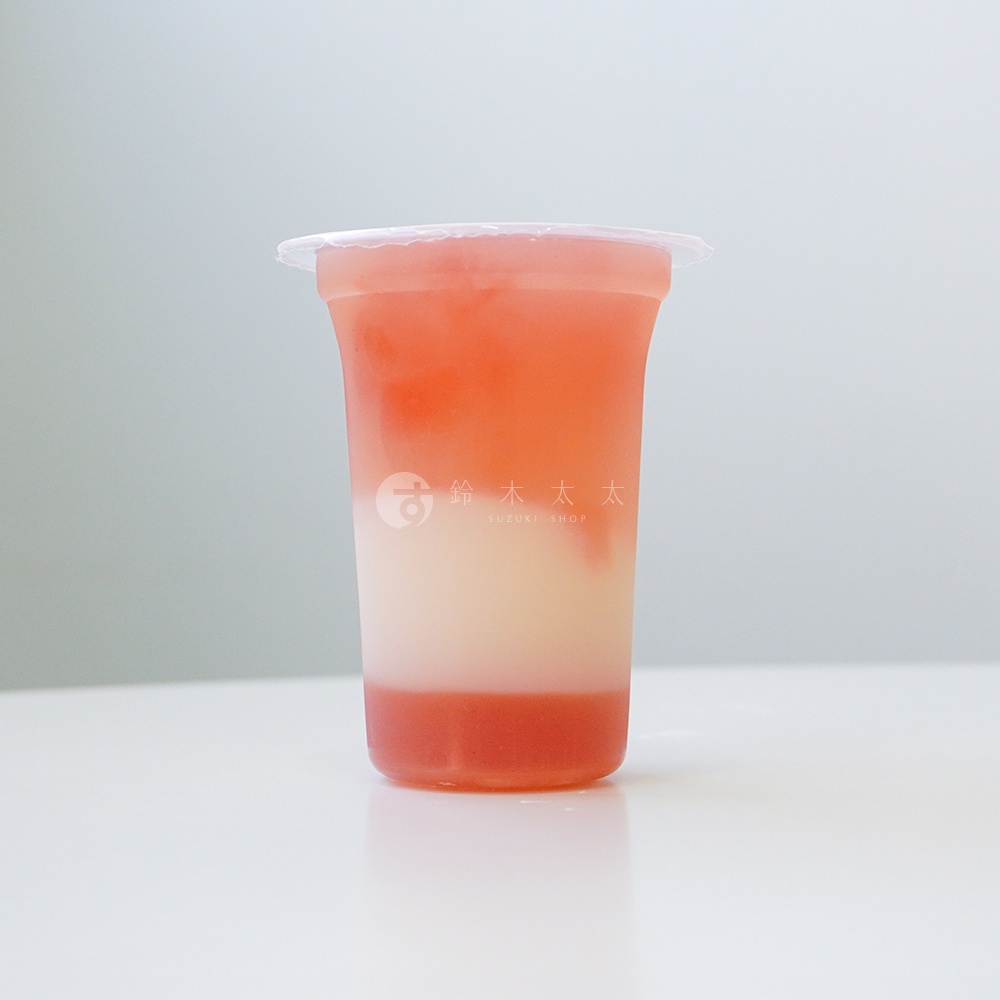透明杯子中裝有三層飲品，底部是紅色果凍，中間為白色奶昔，頂部是粉紅色果汁，杯身印有「鈴木太太」及「SUZUKI SHOP」字樣。