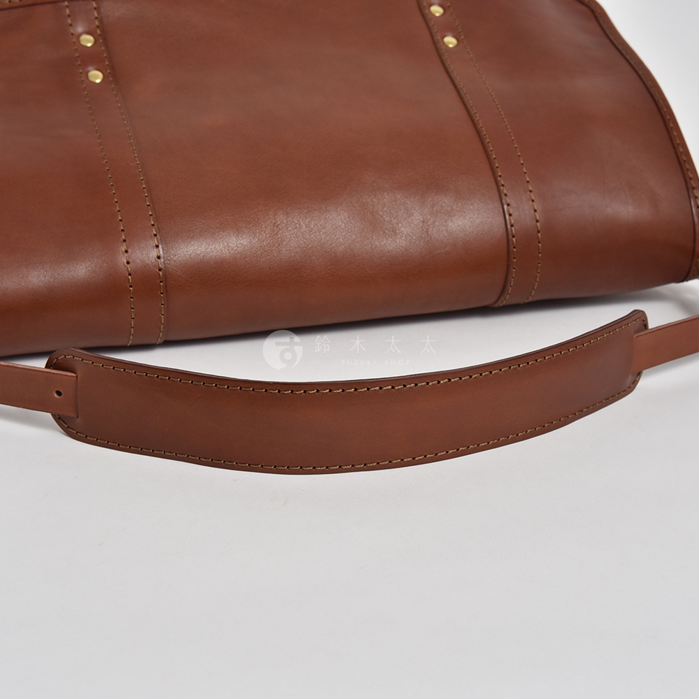 職人手作皮革復古郵差包 CM-100，採用光滑質感棕色皮革製成，包款帶有精緻縫線細節與金屬鉚釘裝飾，肩帶部分可見皮革材質與牢固的車縫。