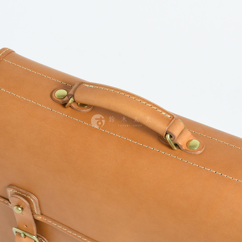 淺棕色皮革手提包，採用手工縫線工藝，配有黃銅色金屬扣件和提把。