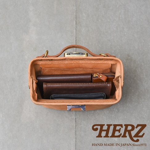 HERZ 職人手作皮革鎖孔式大開口肩背包，內部收納著多個錢包和卡夾，展現精湛工藝。