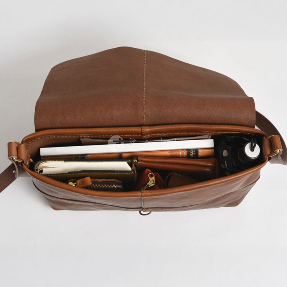 HERZ 品牌職人手作皮革細扣帶馬鞍包，棕色皮革材質，包內裝有筆記本、錢包和一把傘。