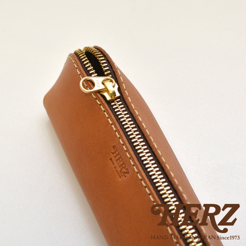 職人手作皮革三角收納筆袋，採淺棕色皮革材質，搭配金色 YKK 拉鍊，縫線整齊，品牌壓印清晰。