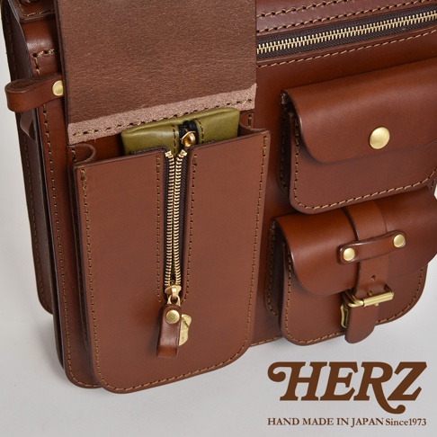 職人手作皮革三口袋三用後背包，採用光滑棕色皮革，設有拉鍊開合的前袋，內有綠色小物，以及兩個帶有金色鈕扣和皮帶扣的翻蓋式口袋。