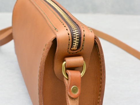 職人手作皮革Organ極簡風拉鍊單肩包 (G-72) M，採用天然棕色皮革製成，搭配金色金屬拉鍊與D型環。包包邊緣有手工縫線，展現職人細膩工藝。