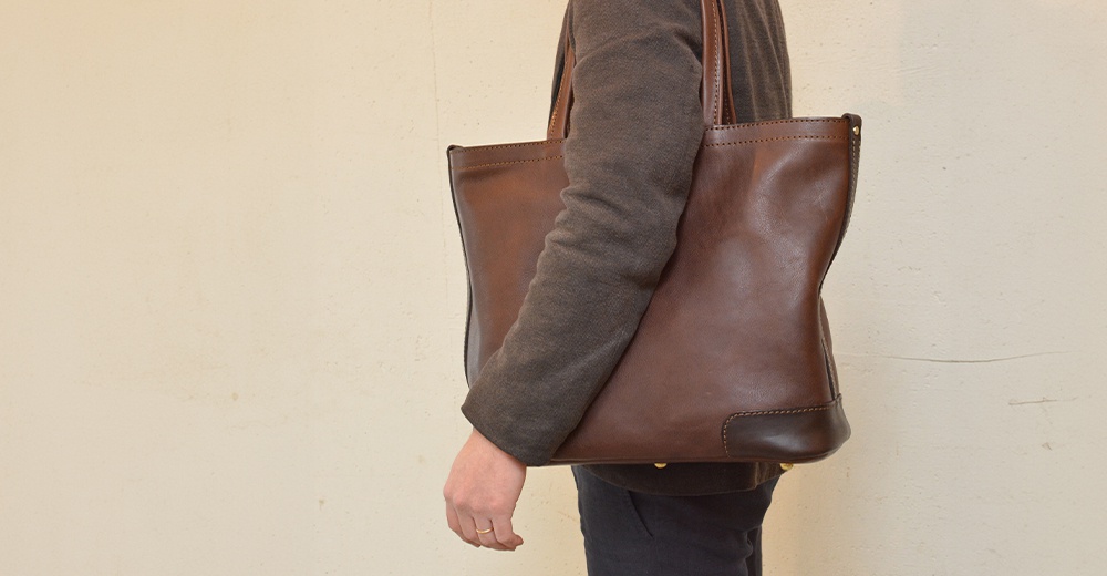 一位身穿棕色外套的女子，肩背著一個深棕色皮革托特包。