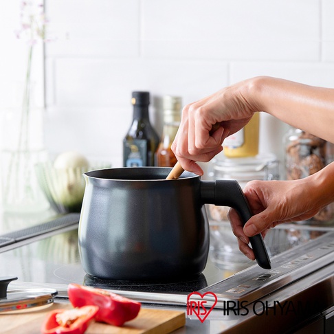 一只手正在用木勺攪拌一個黑色鑽石不沾單柄小湯鍋，鍋放在電磁爐上。