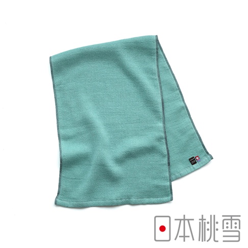 一張淡綠色調的日本桃雪NUGUW今治輕量快乾運動長毛巾，呈現平鋪對折的視角，表面具備細緻的織紋質感，邊緣有灰色縫線修飾，右下角配有象徵今治毛巾品質認證的藍紅圓形標籤及黑色品牌布標。