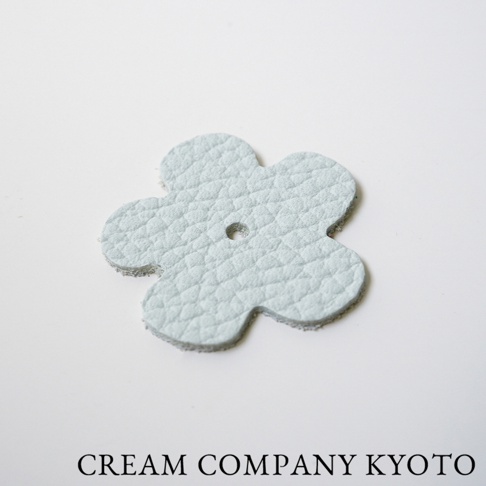 淺藍色皮革製成的五瓣花形吊飾，表面有細緻紋理，中央有圓孔。