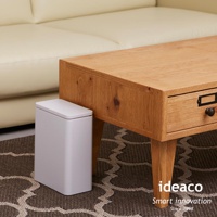 白色簡約方形垃圾桶，設有按壓式開啟的白色頂蓋，置於木質桌子旁的地毯上。