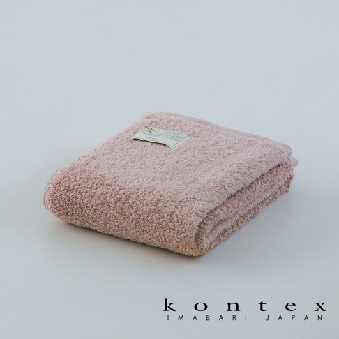 折疊整齊的淡粉色KONTEX品牌毛巾，表面呈現柔軟蓬鬆的毛圈質感，毛巾中央上方貼有一張印有KIYORA產品資訊的精緻標籤，整體畫面簡約優雅，下方標註著KONTEX IMABARI JAPAN字樣。