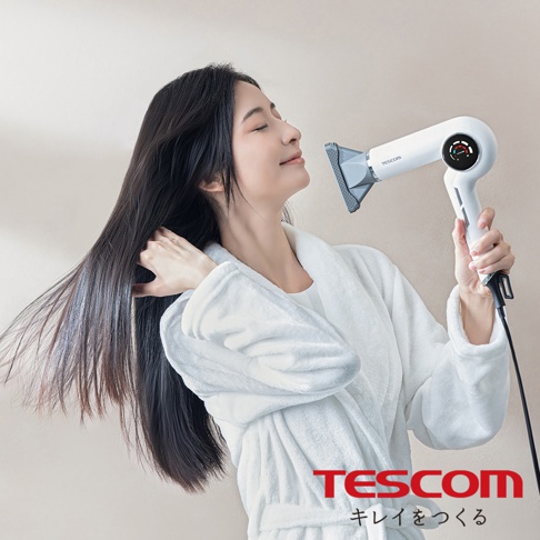 一位女子穿著白色浴袍，手持白色TESCOM吹風機，正在吹乾她烏黑亮麗的長髮。