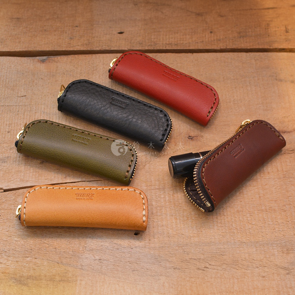 職人手作皮革印章收納袋，展示有紅、黑、墨綠、深棕、淺棕共五種顏色。採用荔枝紋皮革製作，配有金色拉鍊和掛環，整體風格簡約。
