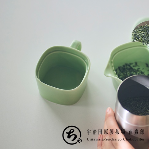 一張特寫照片展示了宇治田原製茶場的淡綠色美濃燒一人用馬克杯，杯身呈現簡約的圓角方型設計，一旁放置著裝有綠茶茶葉的茶具，畫面下方帶有品牌標誌與文字，整體呈現出清新雅緻的沖泡茶飲情境。