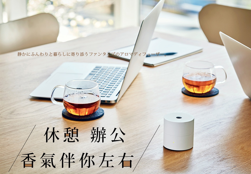 白色圓柱形隨身精油香氛機，頂部有圓孔，下方有一個小黃色指示燈，放置在木質桌面上。